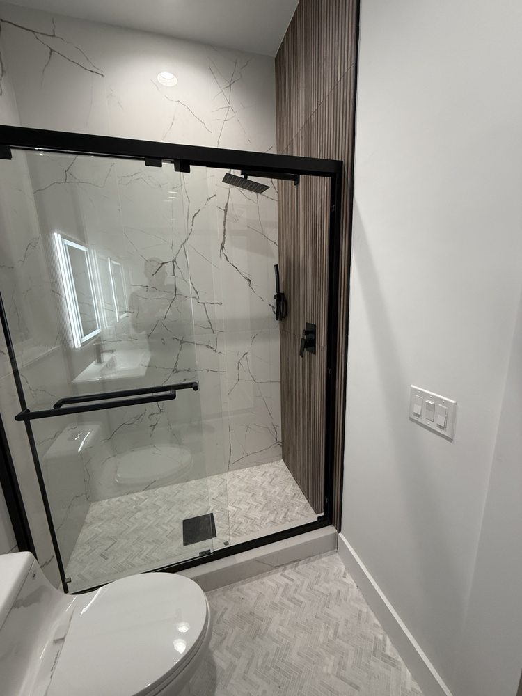 Black-framed sliding glass shower enclosure and marble-look wall tile