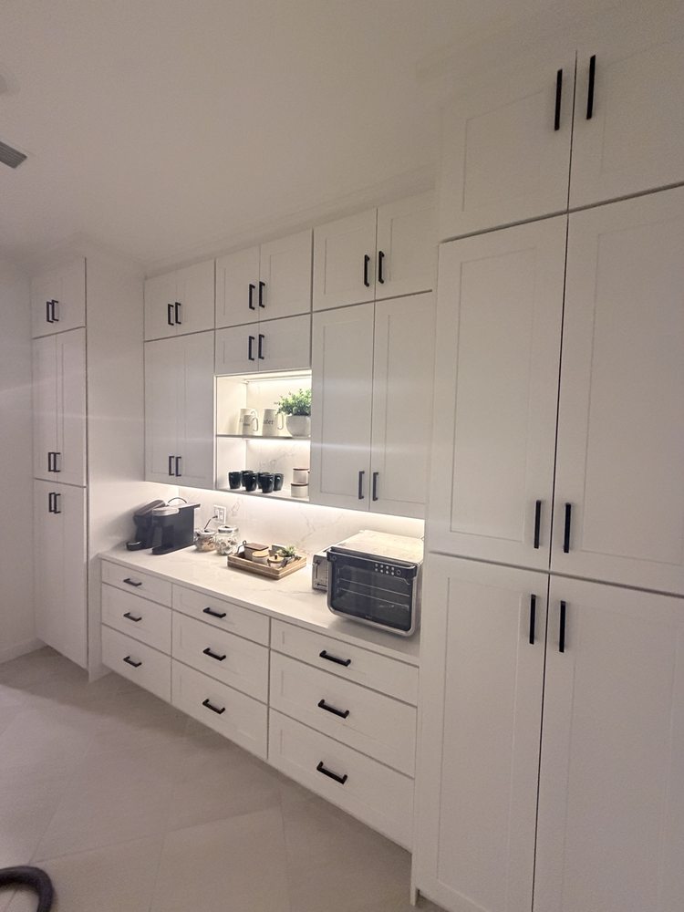 White pantry cabinets with black handles and an illuminated coffee station