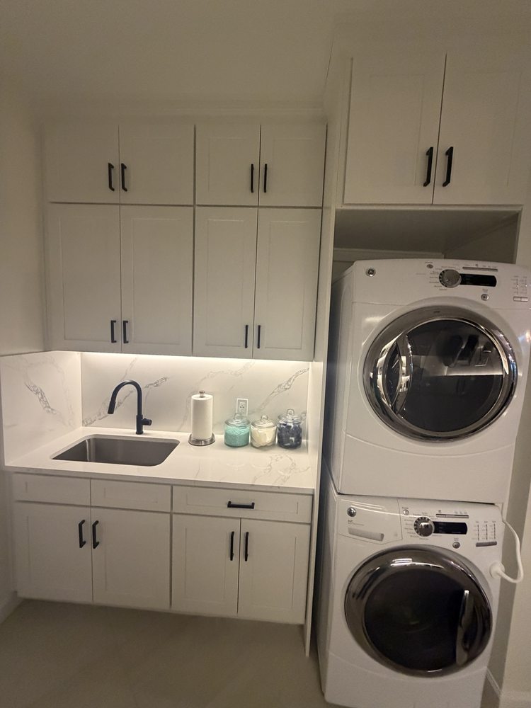 White laundry cabinets, sink and stacked washer and dryer
