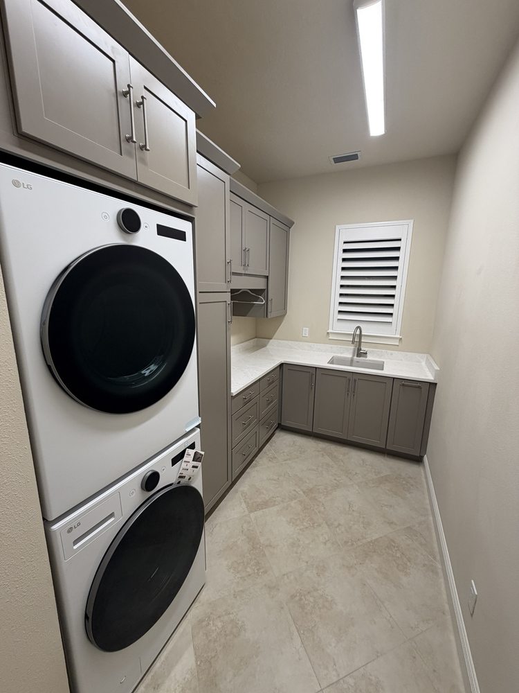 Laundry room with gray cabinets, stacked appliances and a corner sink