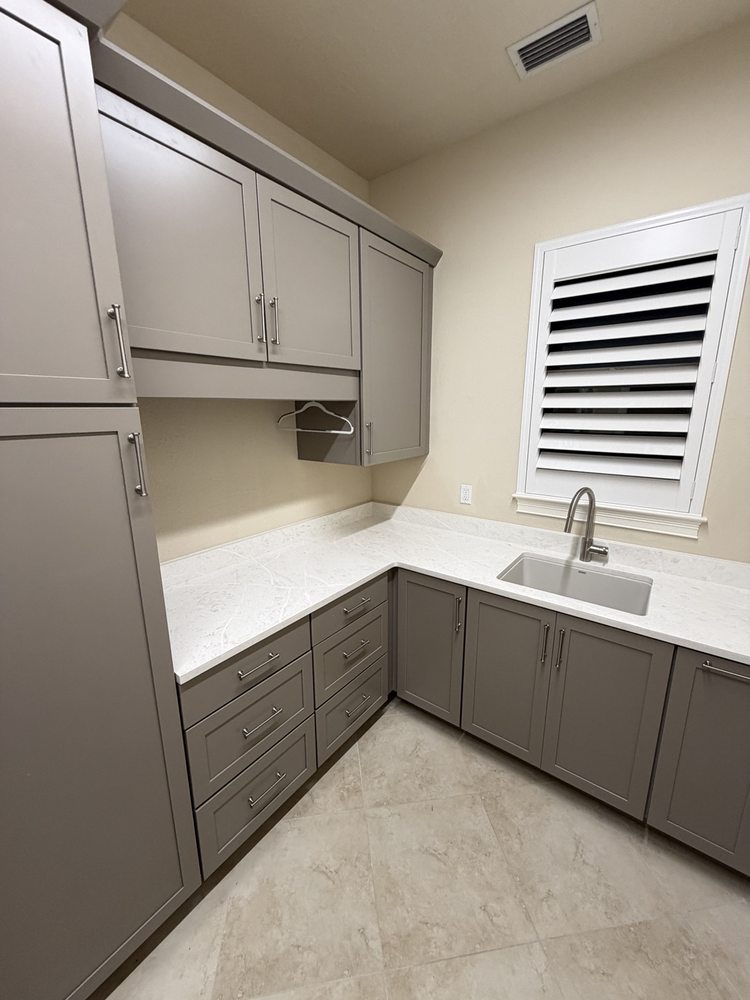 Gray laundry cabinets, drawers and countertop around a corner sink