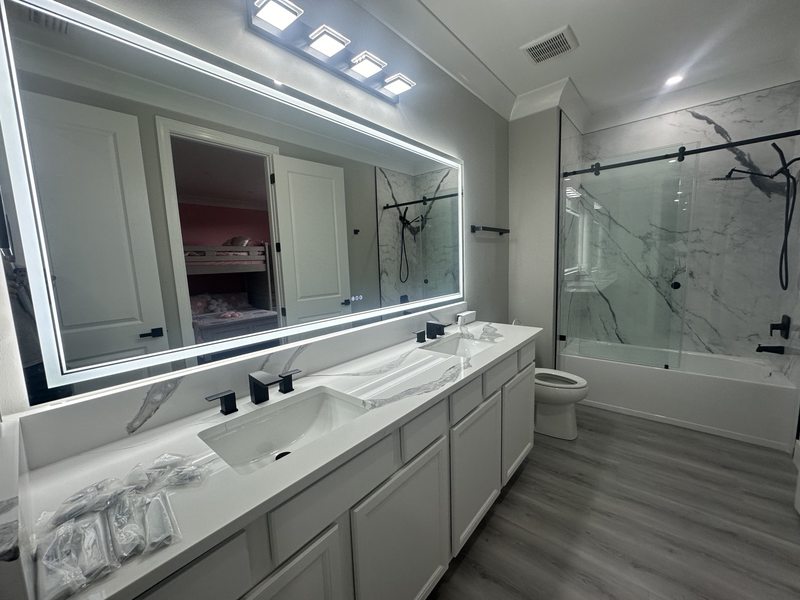 Double vanity with illuminated mirror, shower enclosure and wood-look flooring