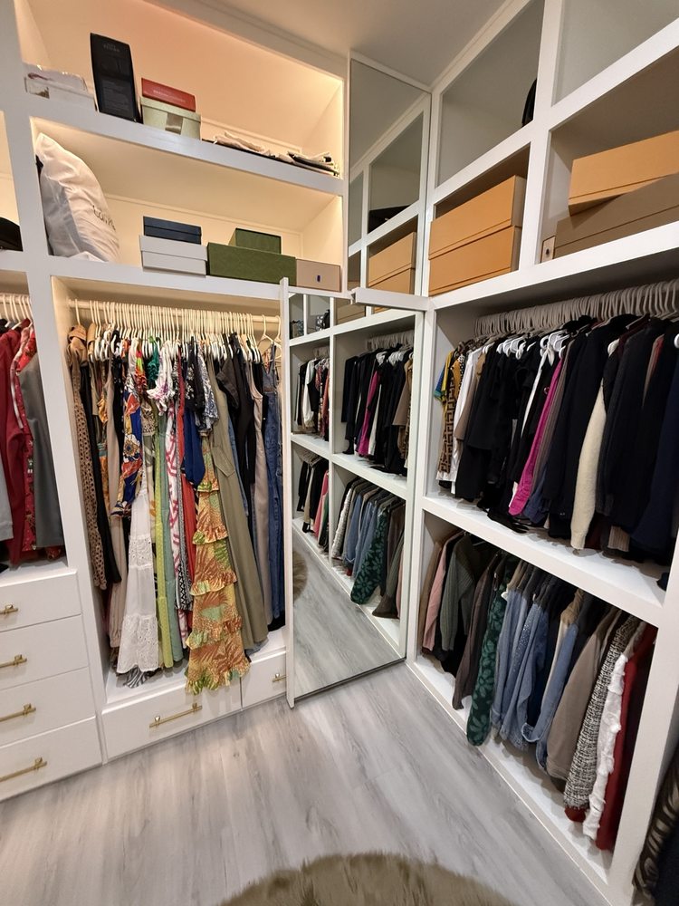 White closet shelving, drawers and hanging rails organizing clothing and storage boxes