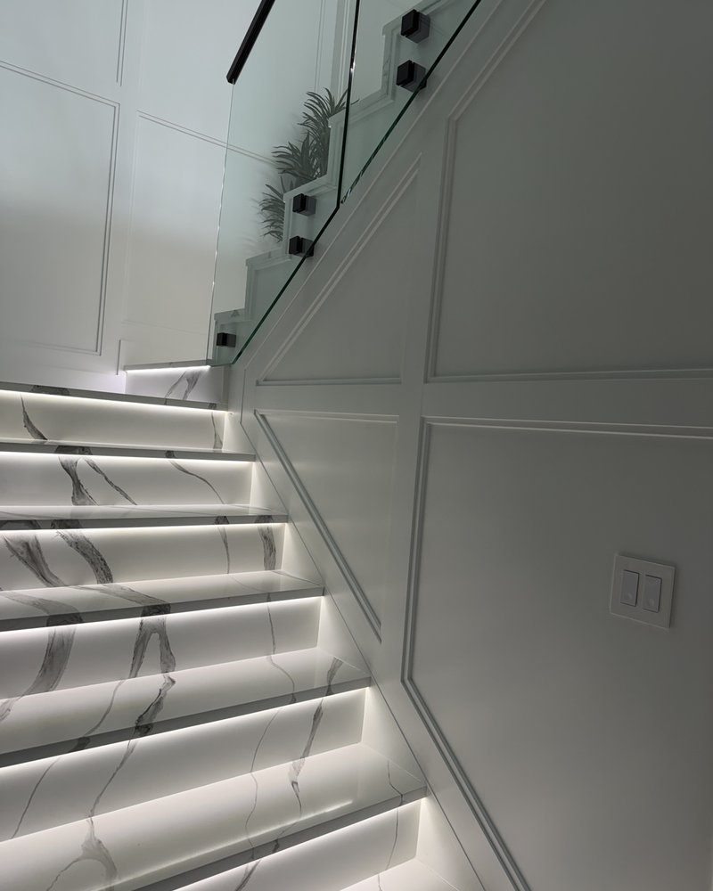 Marble-look staircase with illuminated steps, glass railing and white wall molding