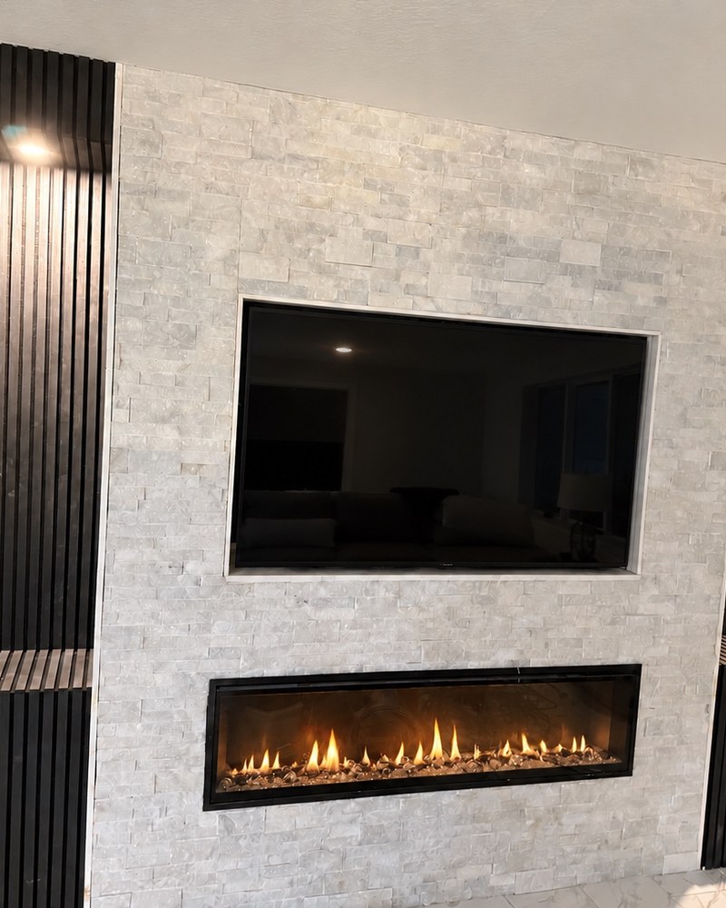 TV and lit fireplace feature wall with white stone, dark slatted panels and illuminated niches