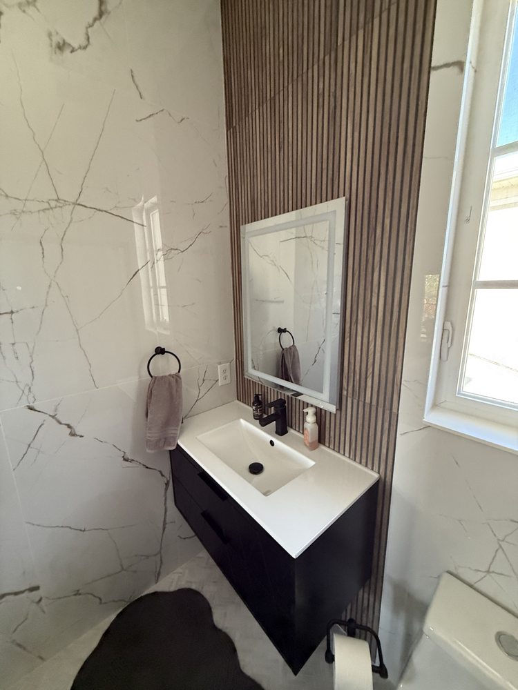 Black vanity against marble-look tile and a slatted accent wall