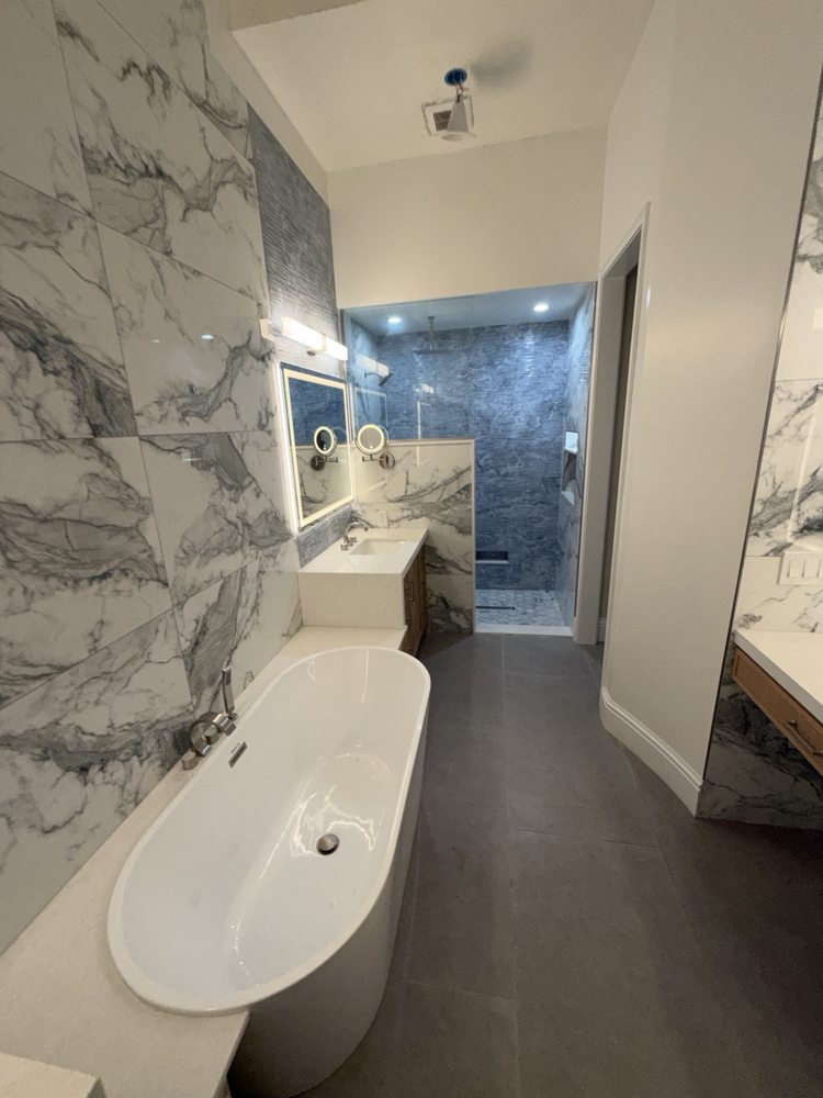Bathroom with a freestanding tub, marble-look wall tile and illuminated vanity mirror