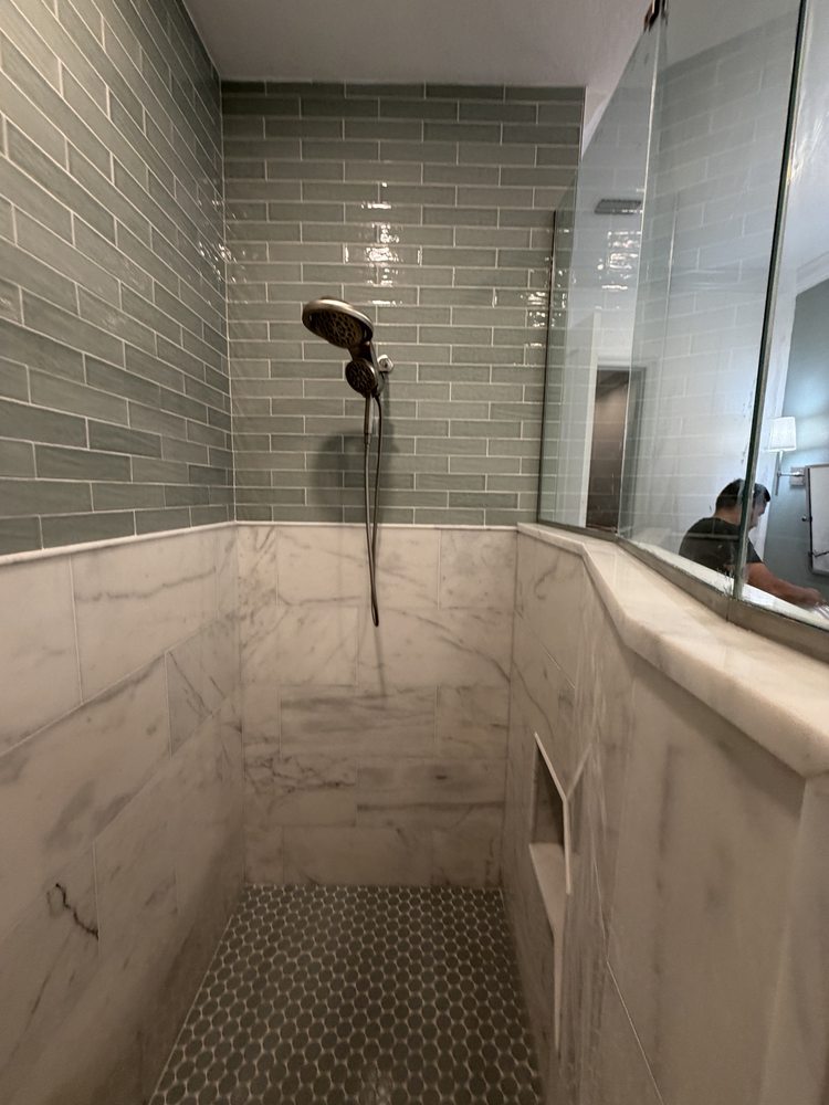 Walk-in shower with green subway tile, marble-look lower walls and mosaic floor