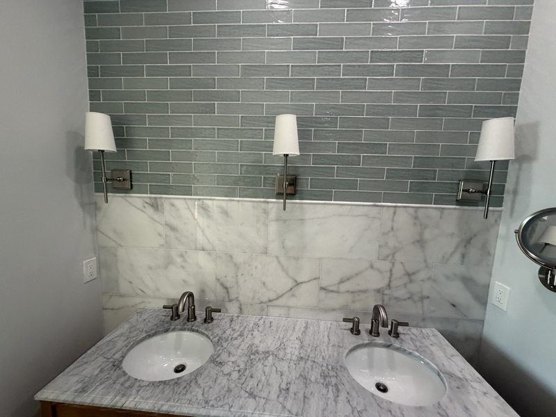 Double-sink vanity with green subway tile and marble-look backsplash