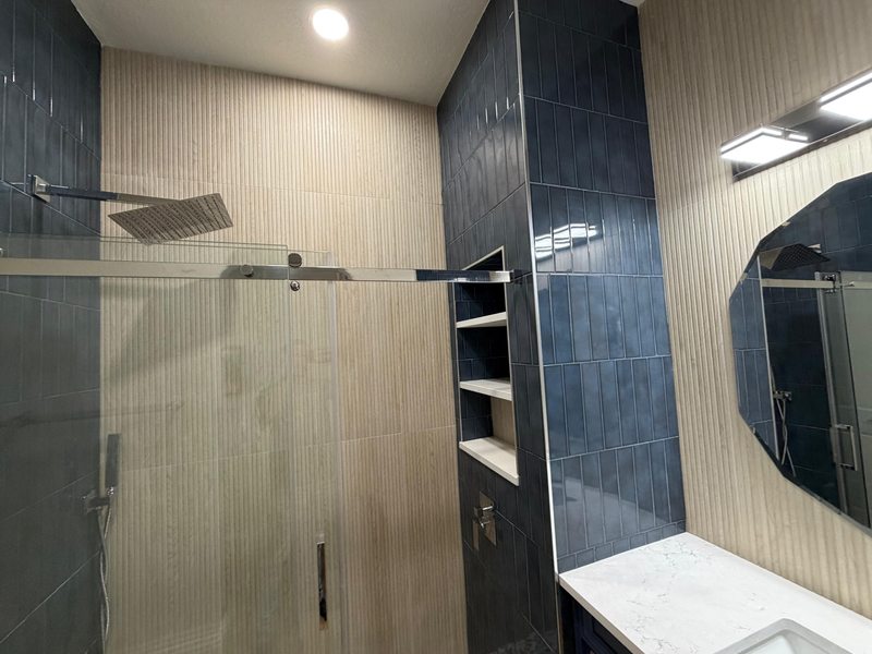 Shower with blue wall tile, textured light walls and recessed shelving