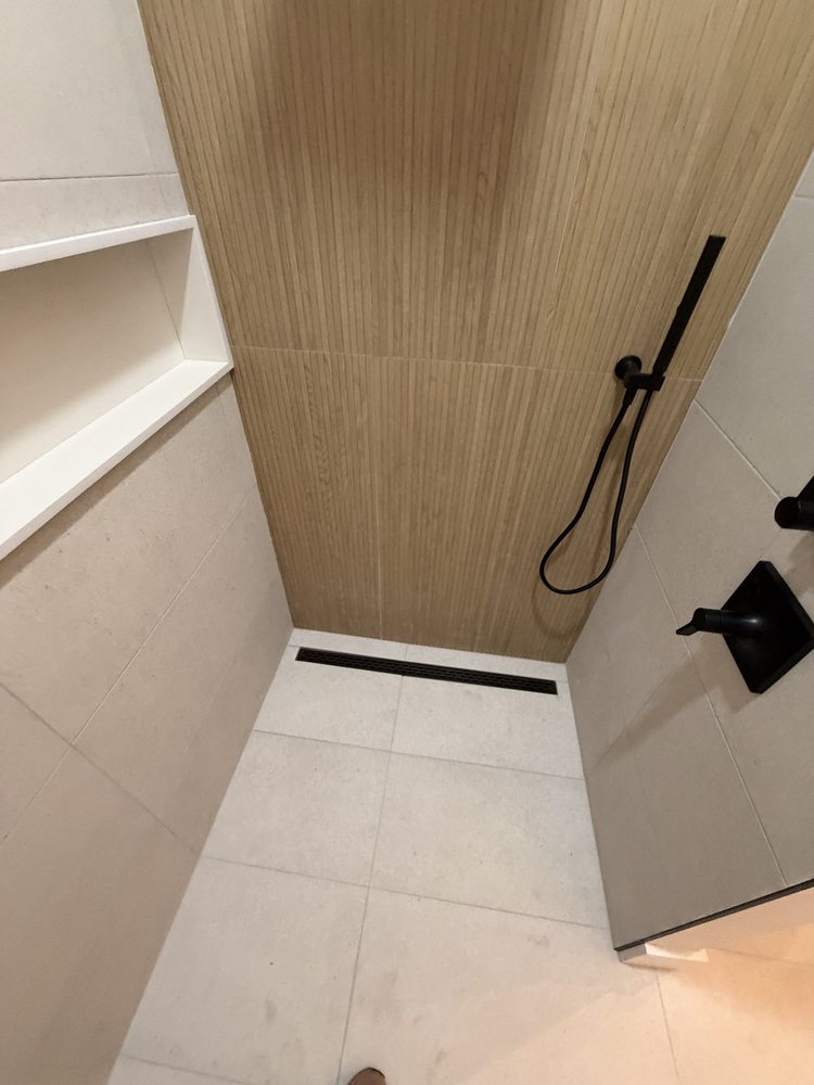 Light tiled shower floor with a black linear drain and handheld shower