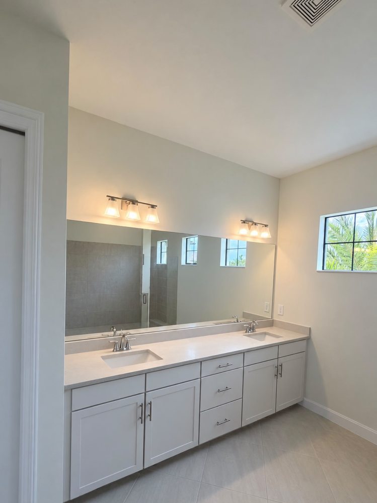 Light double vanity cabinetry with a wide mirror and wall lights