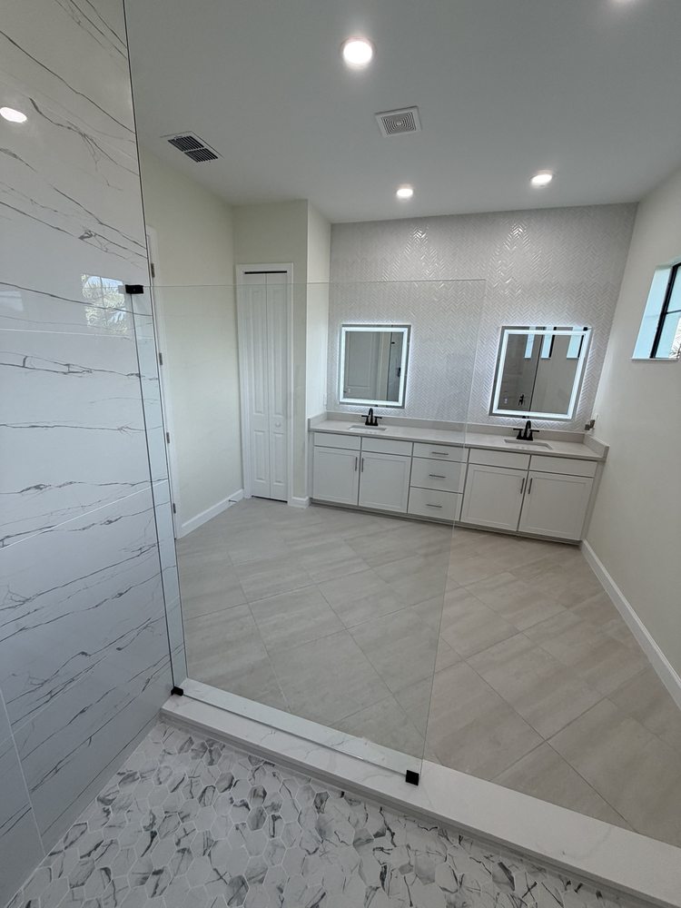 Glass shower panel facing a double vanity with illuminated mirrors