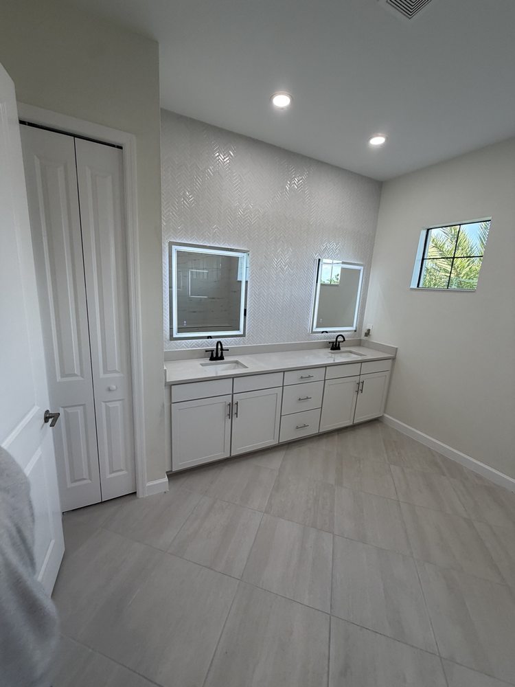 Light double vanity cabinets and illuminated mirrors against a herringbone backsplash