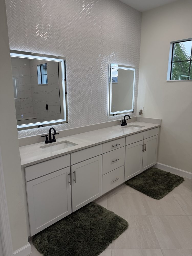 Double vanity, black faucets, illuminated mirrors and herringbone tile backsplash