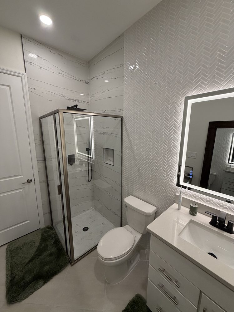 Glass shower enclosure with marble-look tile beside a light bathroom vanity