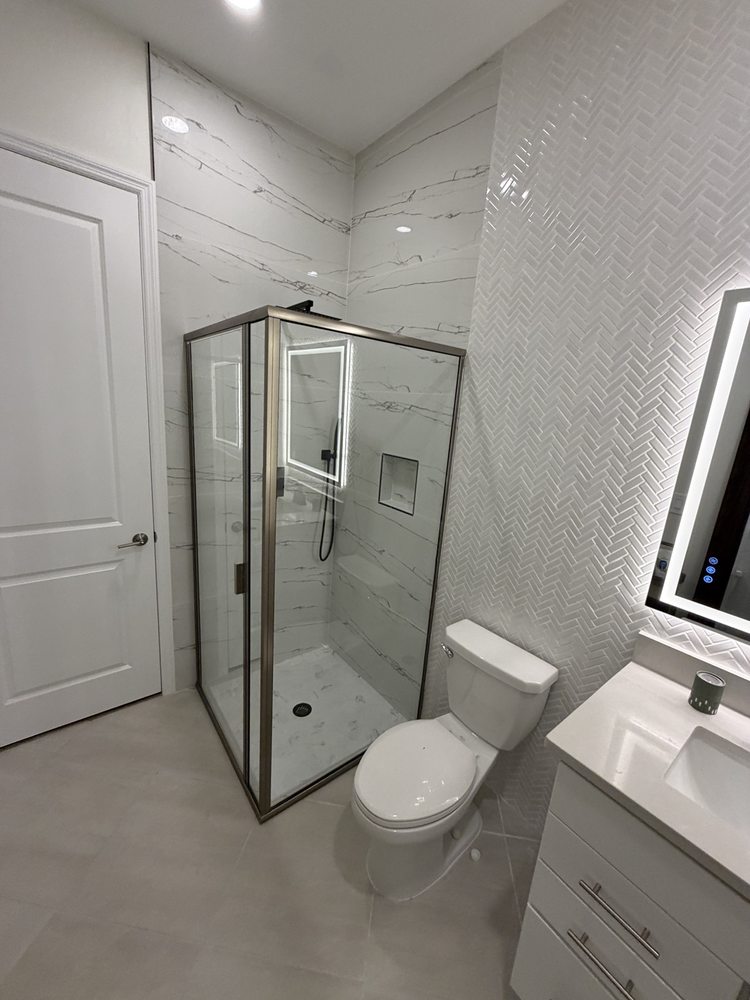 Bathroom with glass shower enclosure, herringbone wall tile and an illuminated mirror