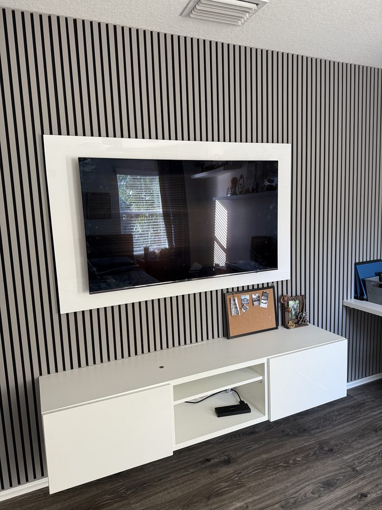 Slatted accent wall with a framed television and floating white cabinet