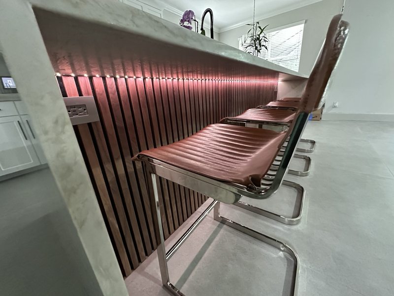 Close view of wood slats and accent lighting beneath a kitchen island countertop